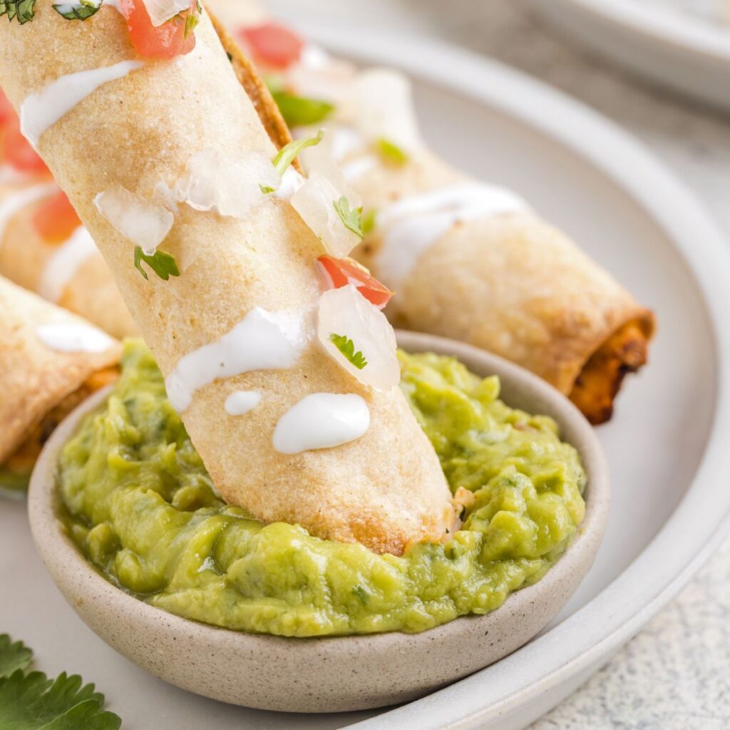 A taquito being dipped into some guacamole. 