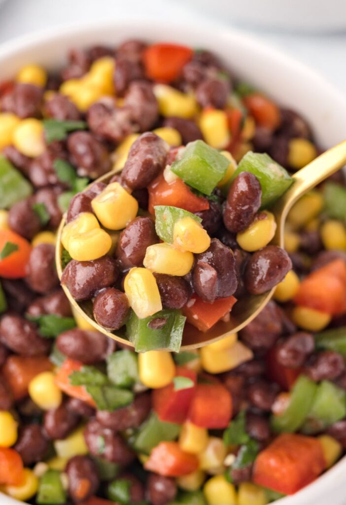 Close up of a golden spoon with some of the salad with black beans and corn on it. 