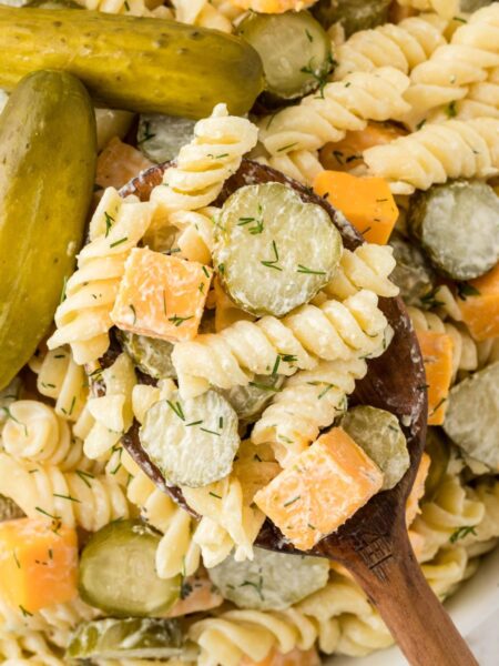 A bowl of this pasta salad with a wooden spoon inside of it.