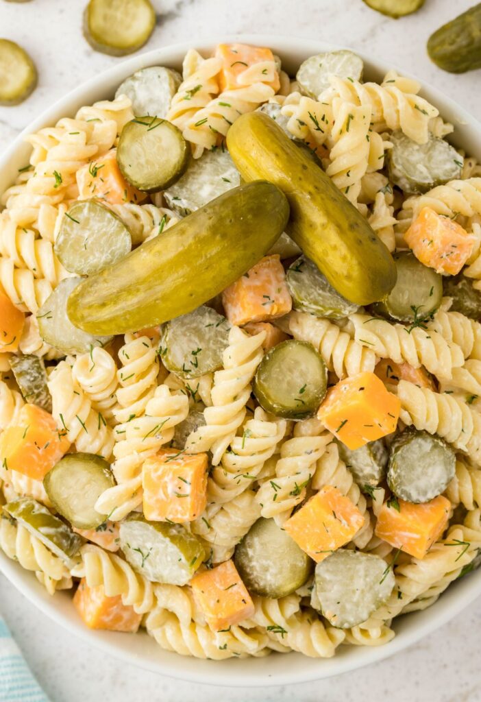 A bowl of pasta salad with whole pickles on top