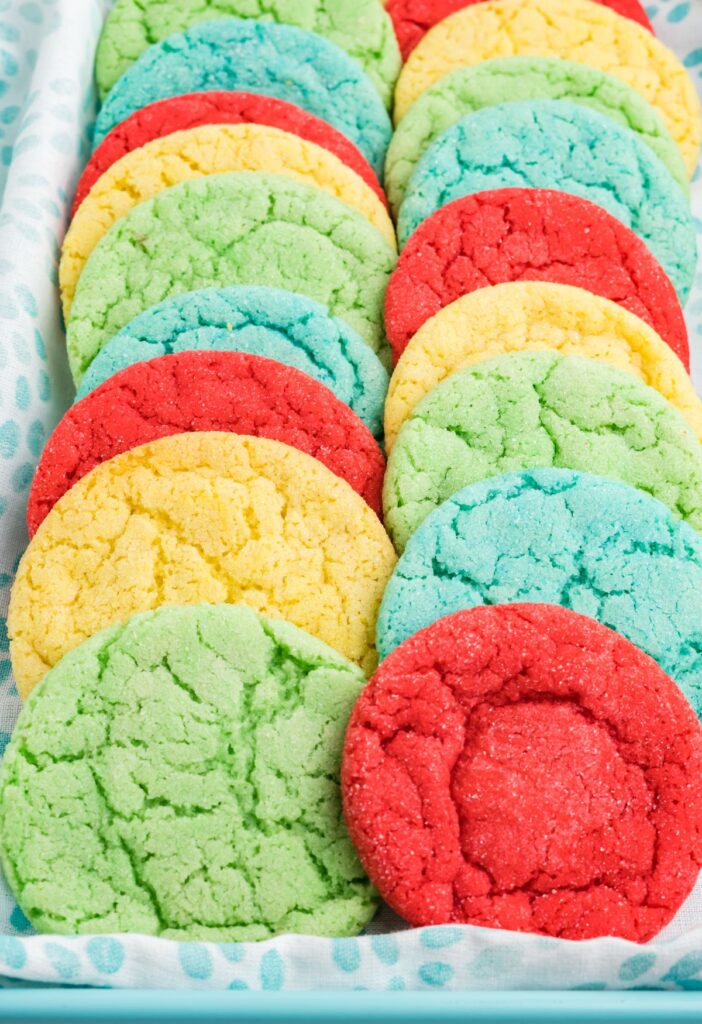 A blue tray with a cloth in it holding rows of colored cookies. 