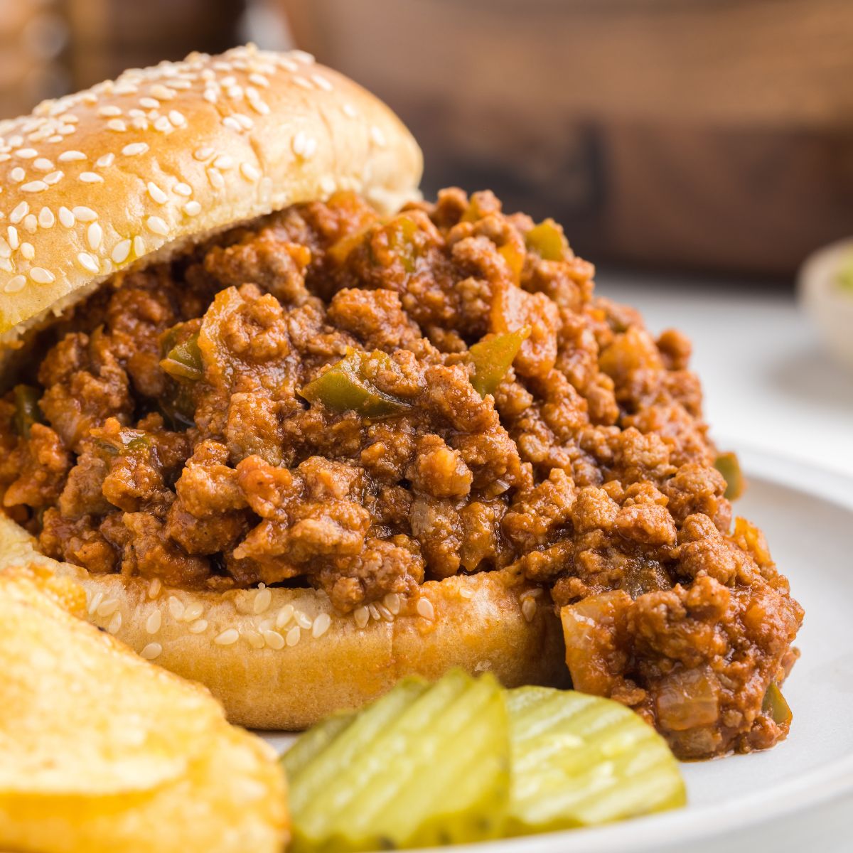 A sloppy Joe sandwich with chips and pickles next to it.