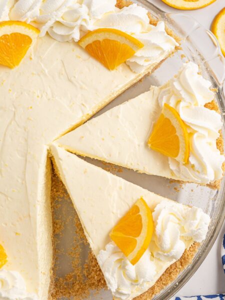 Pie inside a plate with whipped cream and orange slice garnish.