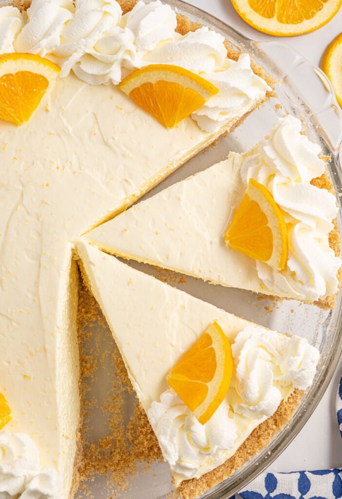 Pie inside a plate with whipped cream and orange slice garnish. 