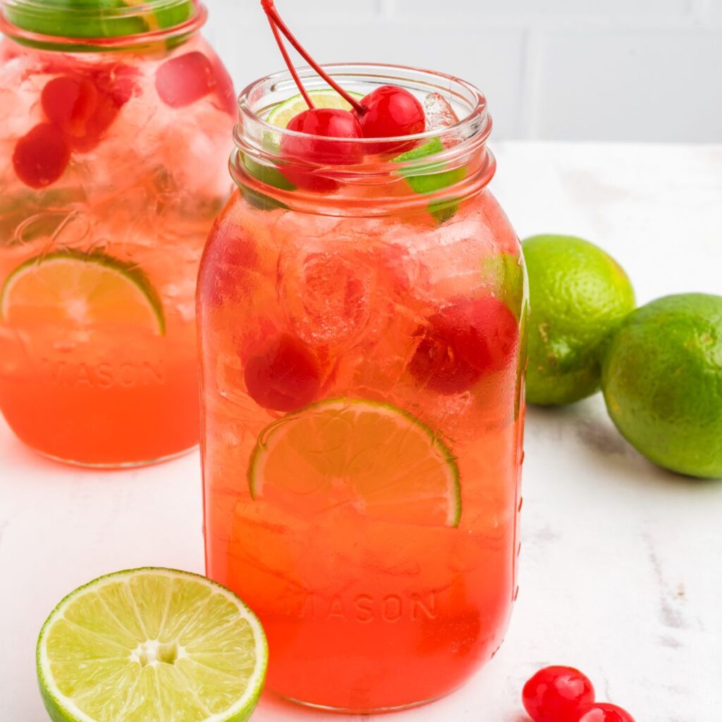 A jar of limeade with cherries and lime wedge beside it. 