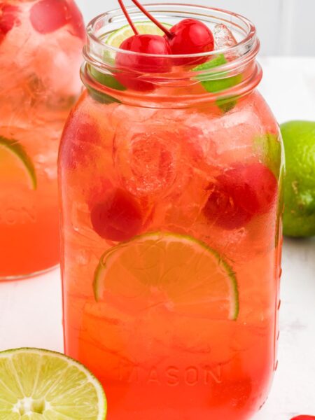 This drink recipe in a glass mason jar topped with cherry and lime wedge.