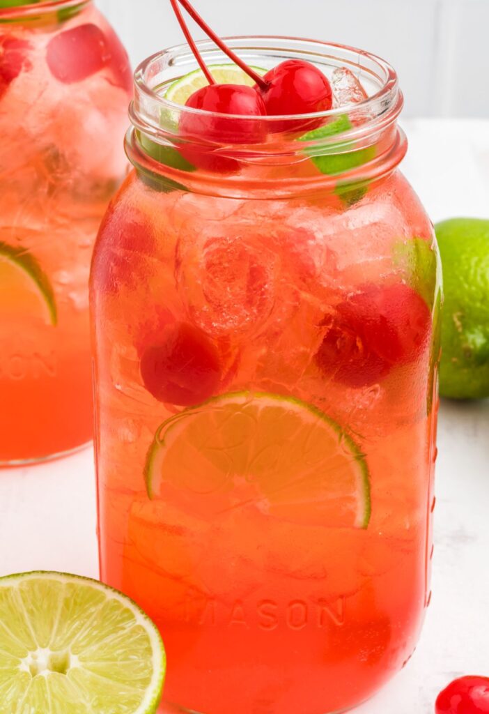 This drink recipe in a glass mason jar topped with cherry and lime wedge. 