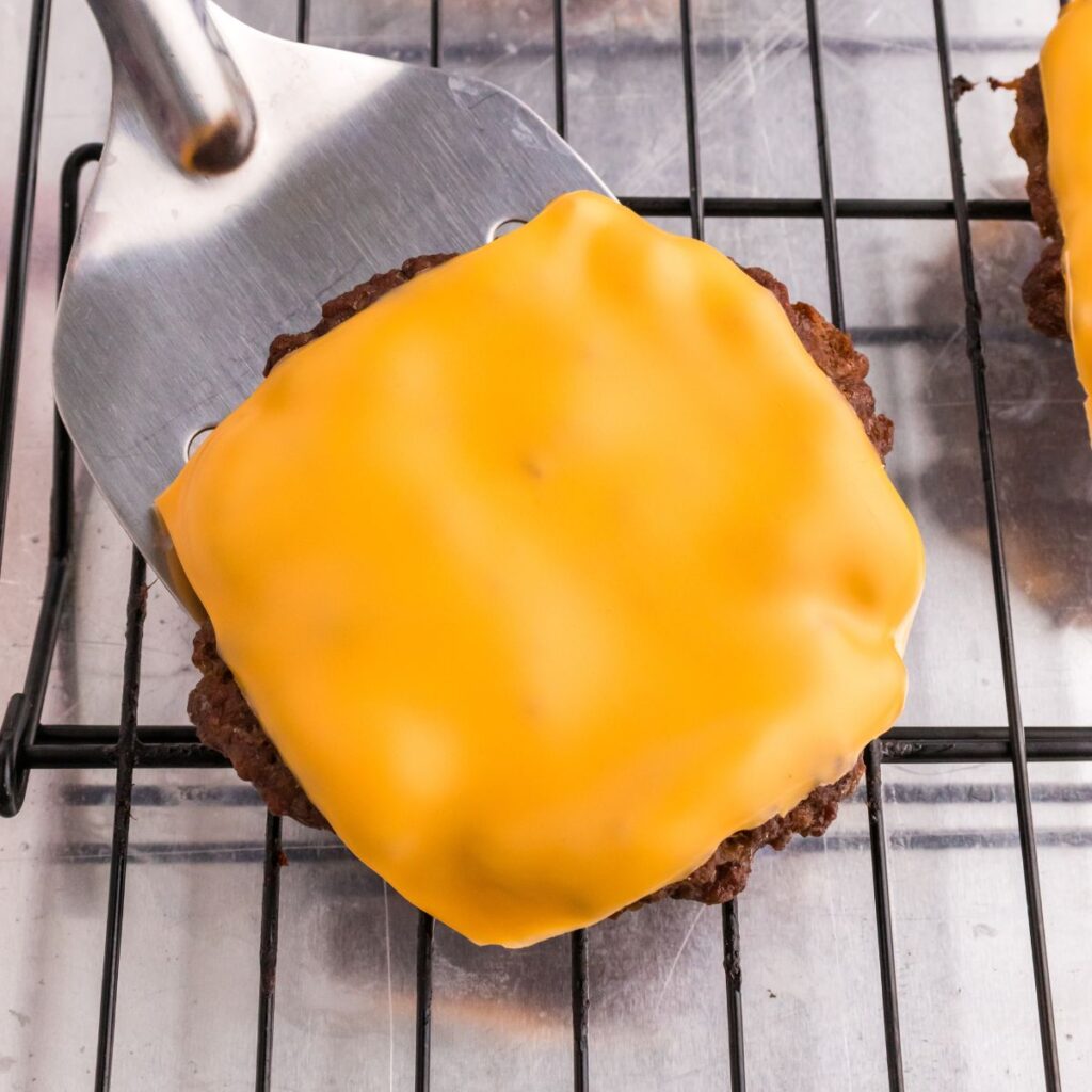 A patty with melted cheese on it on top of a cooling rack. 