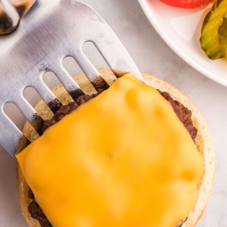A silver spatula putting a burger patty on a bun.