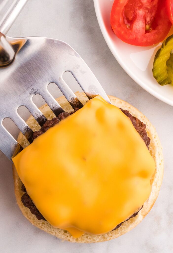 A silver spatula putting a burger patty on a bun. 