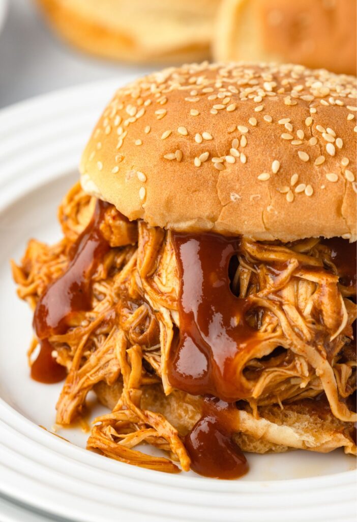 A barbecue chicken sandwich with extra sauce pouring over it. 