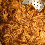 A crock pot full of shredded barbecue chicken in it.