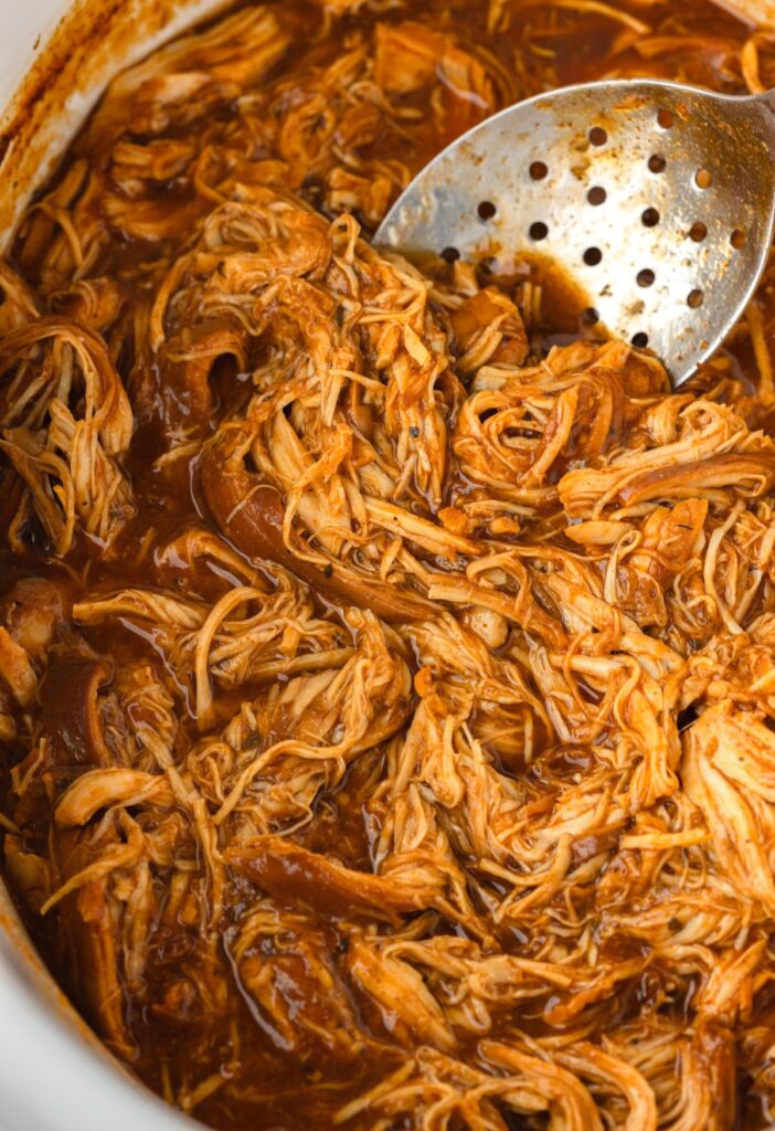 A crock pot full of shredded barbecue chicken in it.