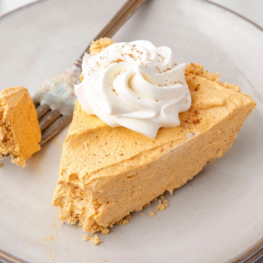Slice of this pumpkin fluff pie on a plate with a fork and whipped cream. 