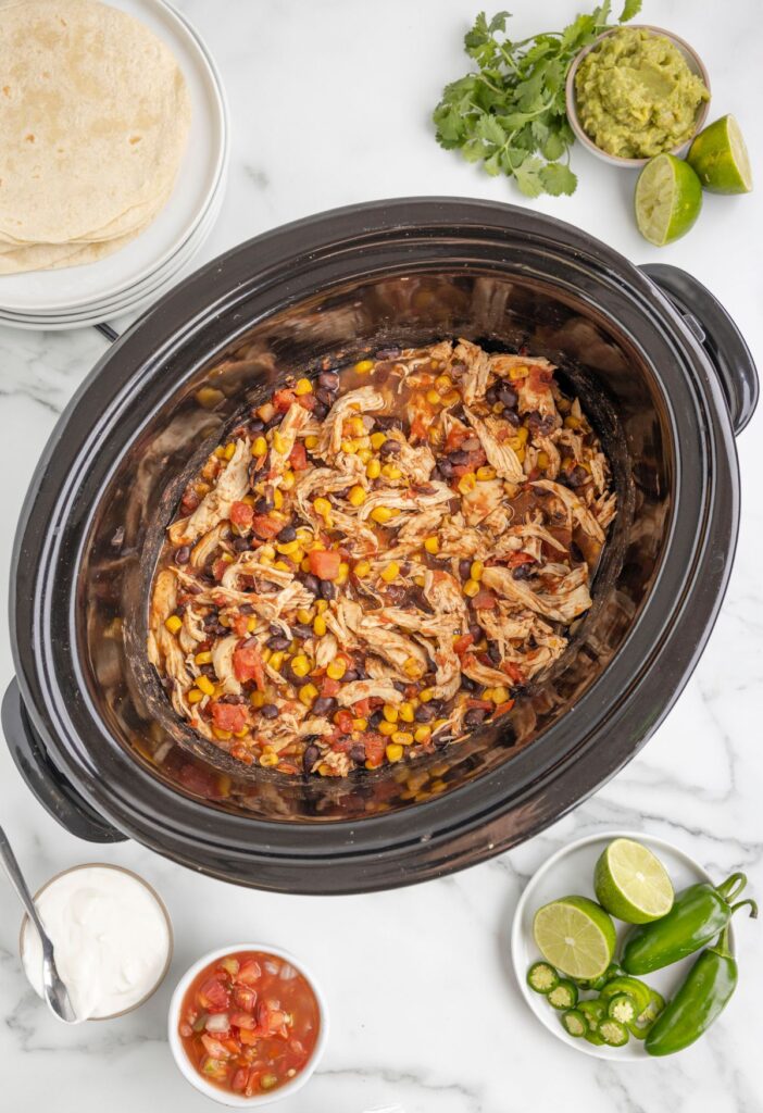 Overhead of the insert of the slow cooker with the tortillas and taco toppings around it. 