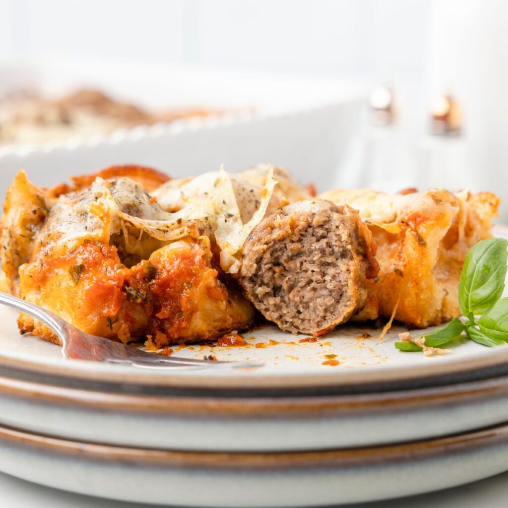 A serving of this casserole on a plate with a meatball cut in half. 