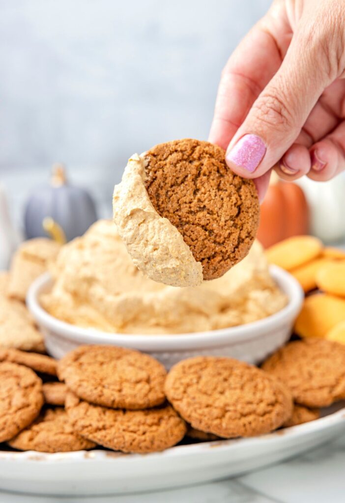 A hand holding a cookie and dipping it into the fluff dip. 