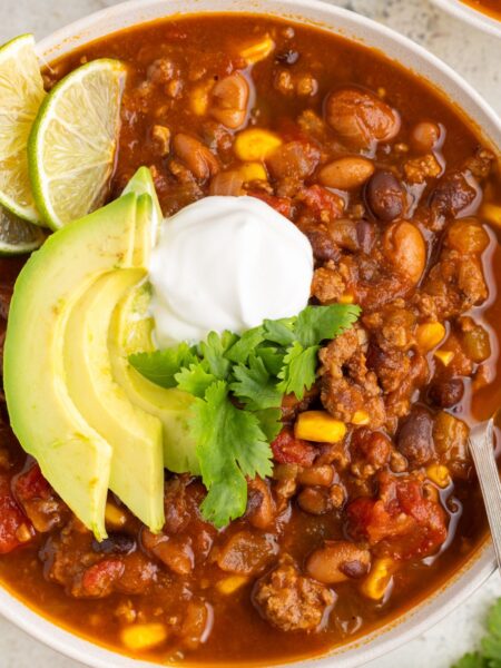 A white bowl of soup with toppings like sour cream and avocado.