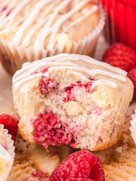 A muffin with a bite out of it against a red dish and fresh raspberries.